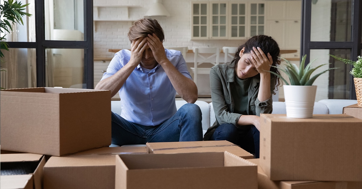 Exhausted young couple sit rest on sofa in living room near heap of cardboard boxes feel unmotivated to unpack their belongings.