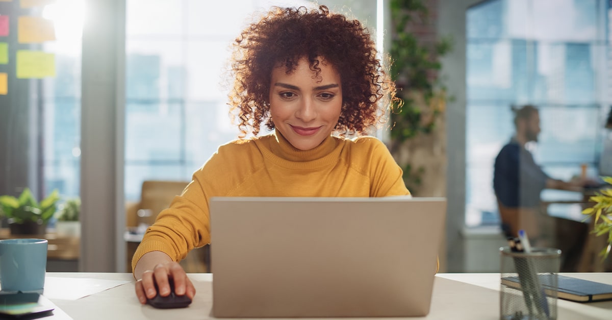 Close Up Portrait of a Happy Female Manager Sitting at a Desk in an Office. Young Stylish Female with Curly Hair Using Laptop Computer