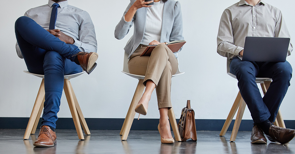 Male and female professionals sitting in front of a wall, cropped and only showing legs as they sit in a waiting room for hiring process, interview in Portuguese