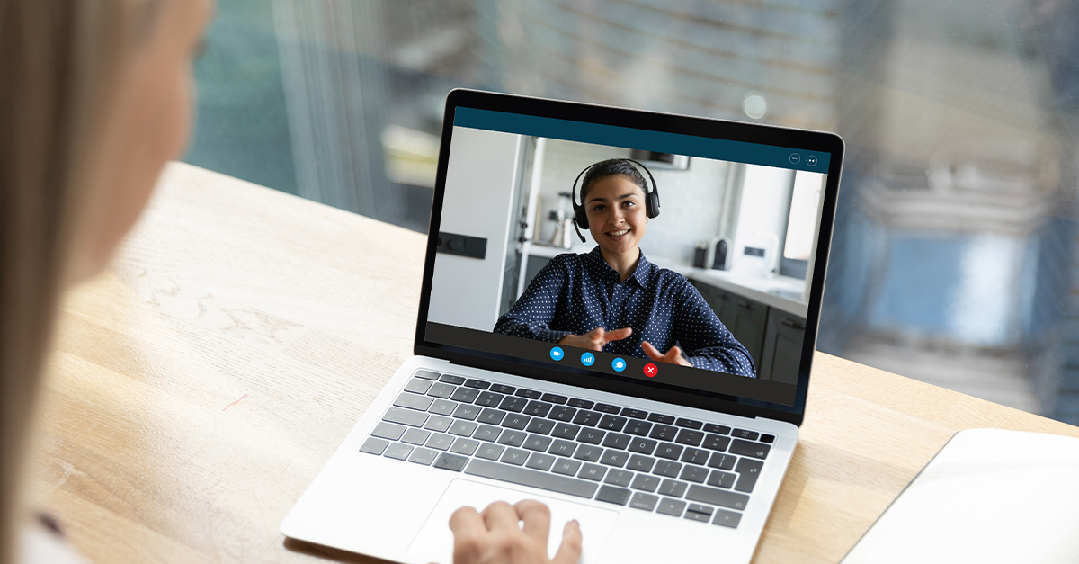 Close up rear view businesswoman chatting with female Indian teacher online, using laptop and webcam, sitting at table in office. Personal Language Coaching