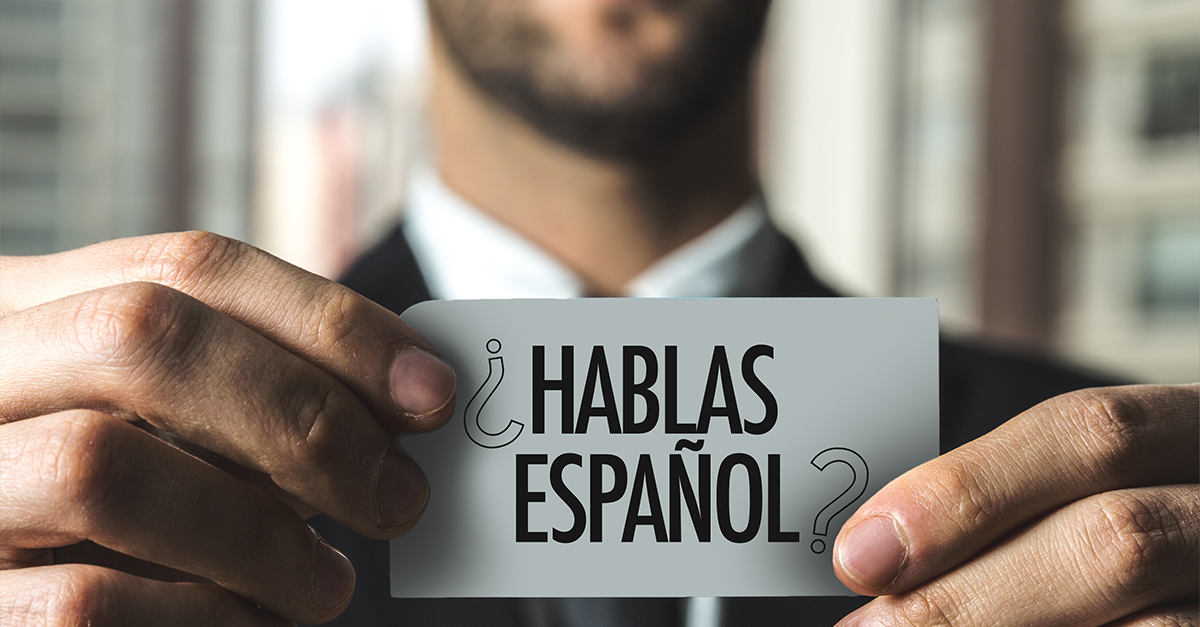 Business man holding a card with both hands in the foreground that reads Hablas Espanol? (Do You Speak Spanish?)