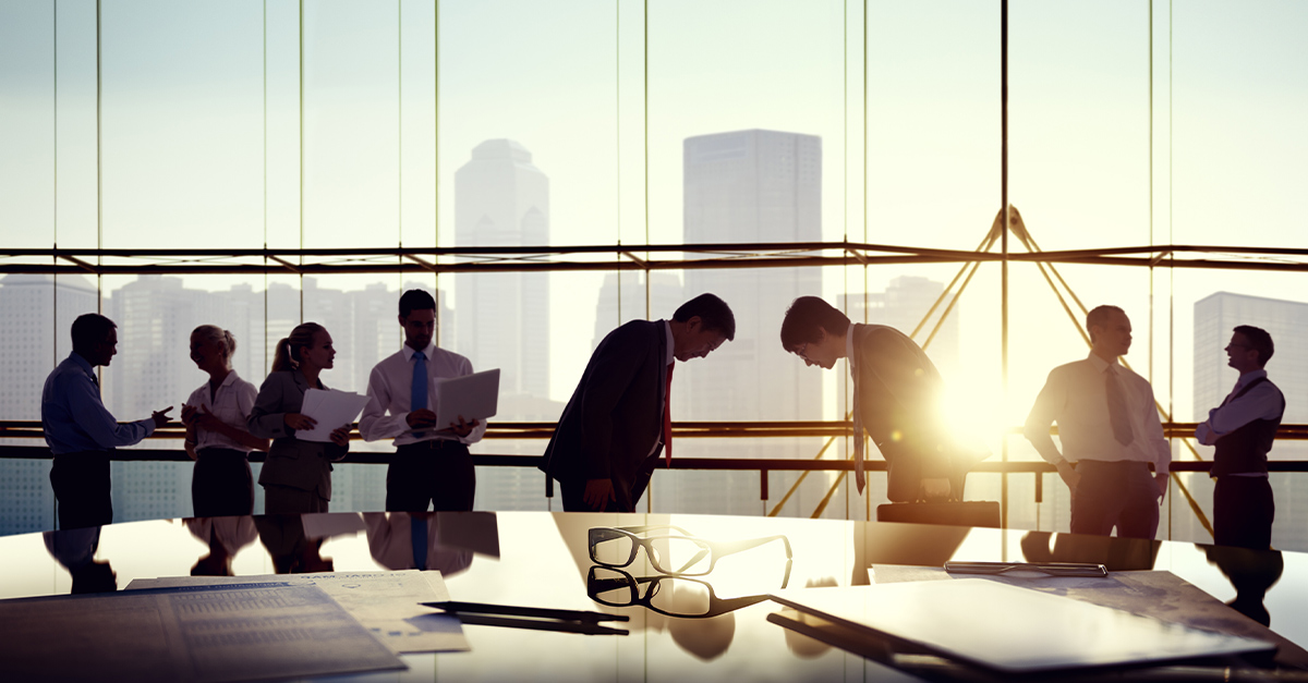 Group of business people talking and two men bowing reflected onto table with documents depicting differences between Japanese and American cultures