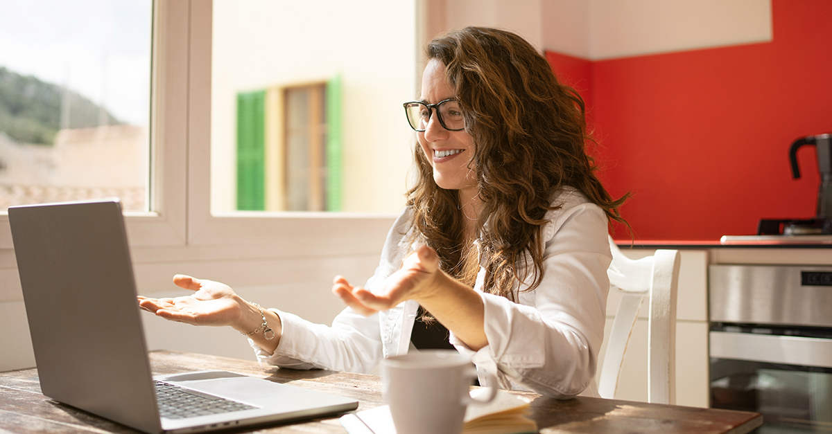 Woman gesturing at her laptop screen with both hands, palms up, and smiling, while working with a corporate language coach, illustrating the blog topic "Getting Back to Spanish for Your Career: A Practical Guide"