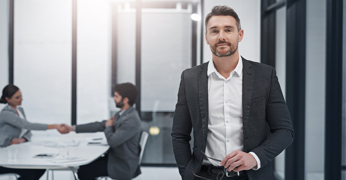 Executive in foreground of conference room with two employees in the background, seated and shaking hands across the table. Language Learning is crucial for Executives in today's global workforce
