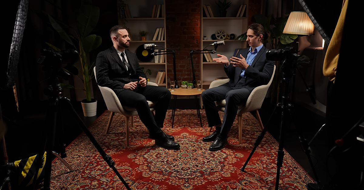 Two male professionals speaking on a podcast in a darkened studio