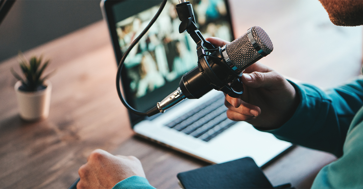 A man host streaming his audio podcast using microphone and laptop at his small broadcast studio, close-up