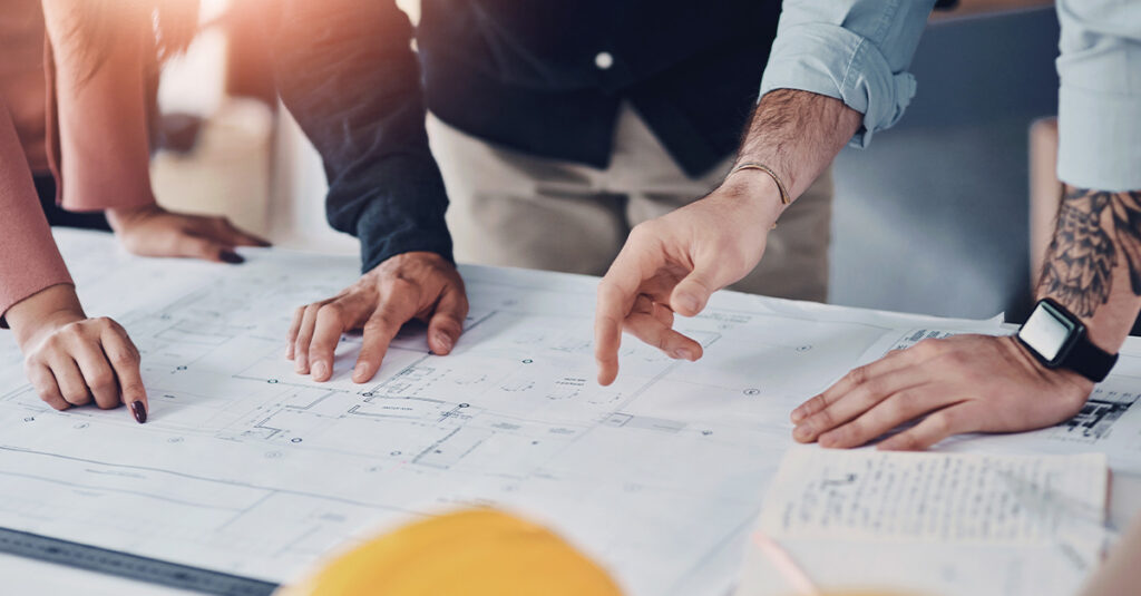 Blueprints on a table with the hands of architects shown gesturing to different parts illustrating the blog topic of Spanish for Architects