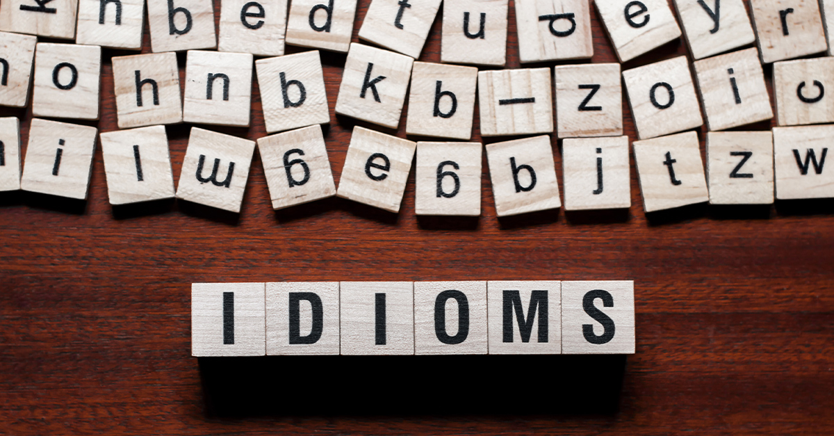 Idioms word concept on small wooden tiles on a dark wood background