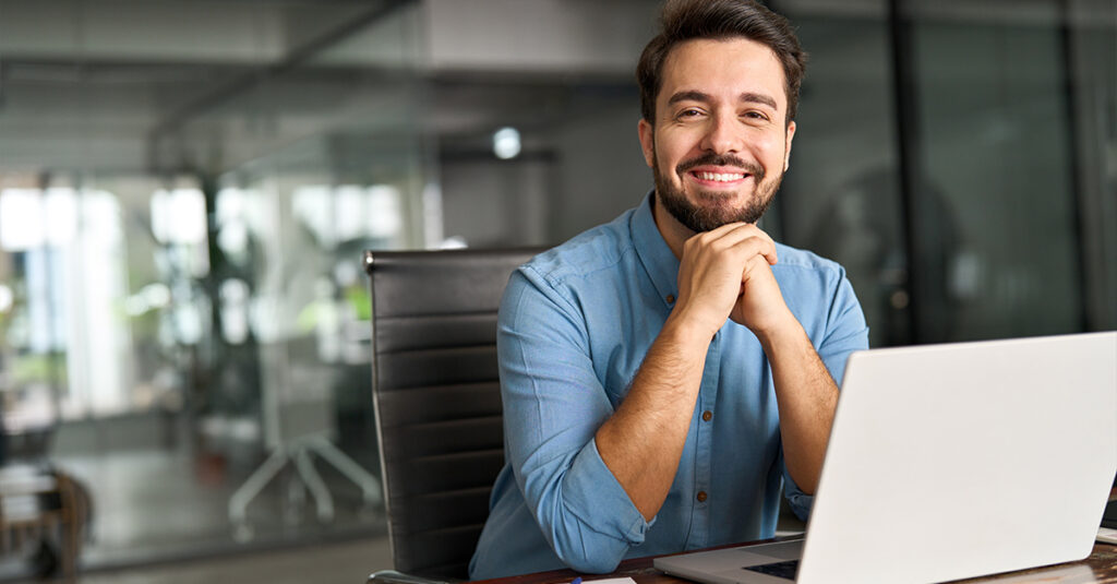 Male professional in front of a computer smiling at the camera illustrating the blog topic Using Substack as a Language Learning Resource