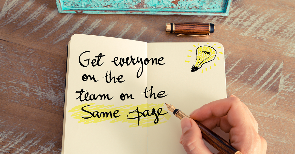 Retro effect and toned image of a woman hand writing a note with fountain pen on a notebook. Written text GET EVERYONE ON THE TEAM ON THE SAME PAGE next to yellow lighting bulb as symbol for idea, illustrating the blog topic of Business English Idioms
