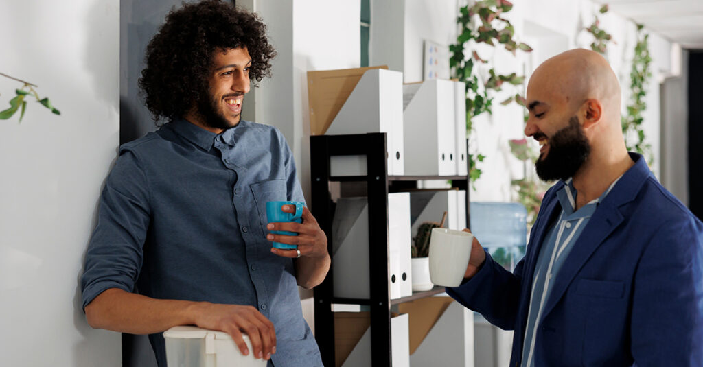 Businessmen enjoying coffee break together and laughing while relaxing in corporate office, illustrating the blog topic Laugh Your Way to Fluency: The Power of Humor in Language Learning