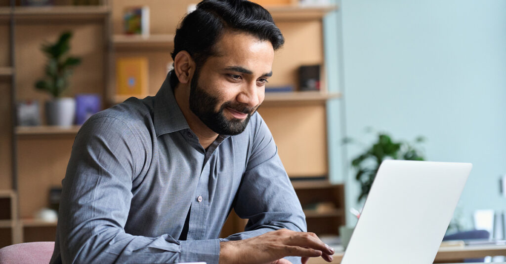 Smiling man working on laptop, illustrating the blog topic Free Resources to Learn Business English
