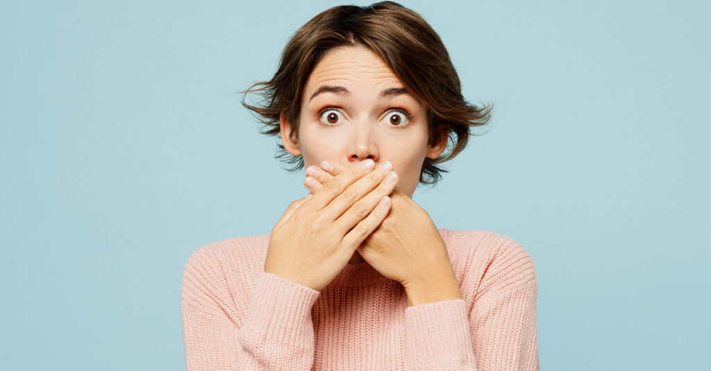 Close up of a young woman with her hands covering her mouth and an embarrassed expression, illustrating the blog topic "Spanish Words You Should Avoid in a Business Environment"