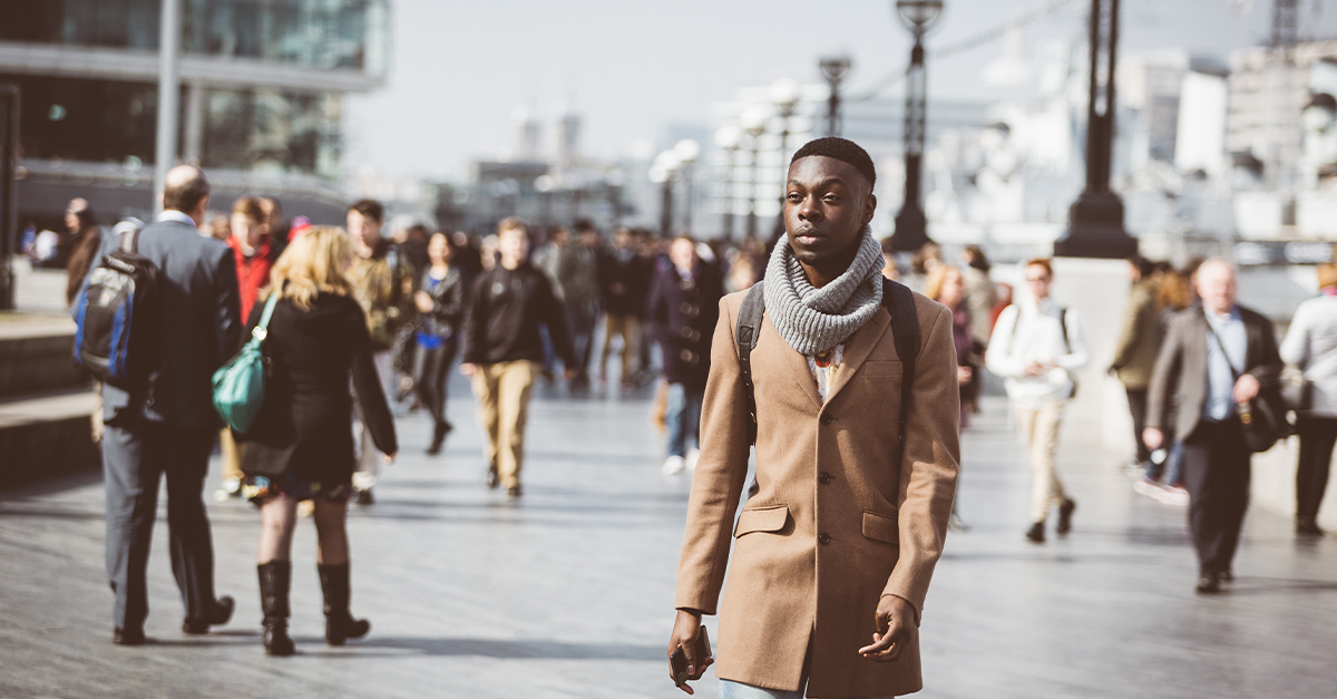 Man walking in London on Thames sidewalk, with blurred people on background. He is looking away. Photo taken on a sunny winter day. Living abroad in an English-speaking country
