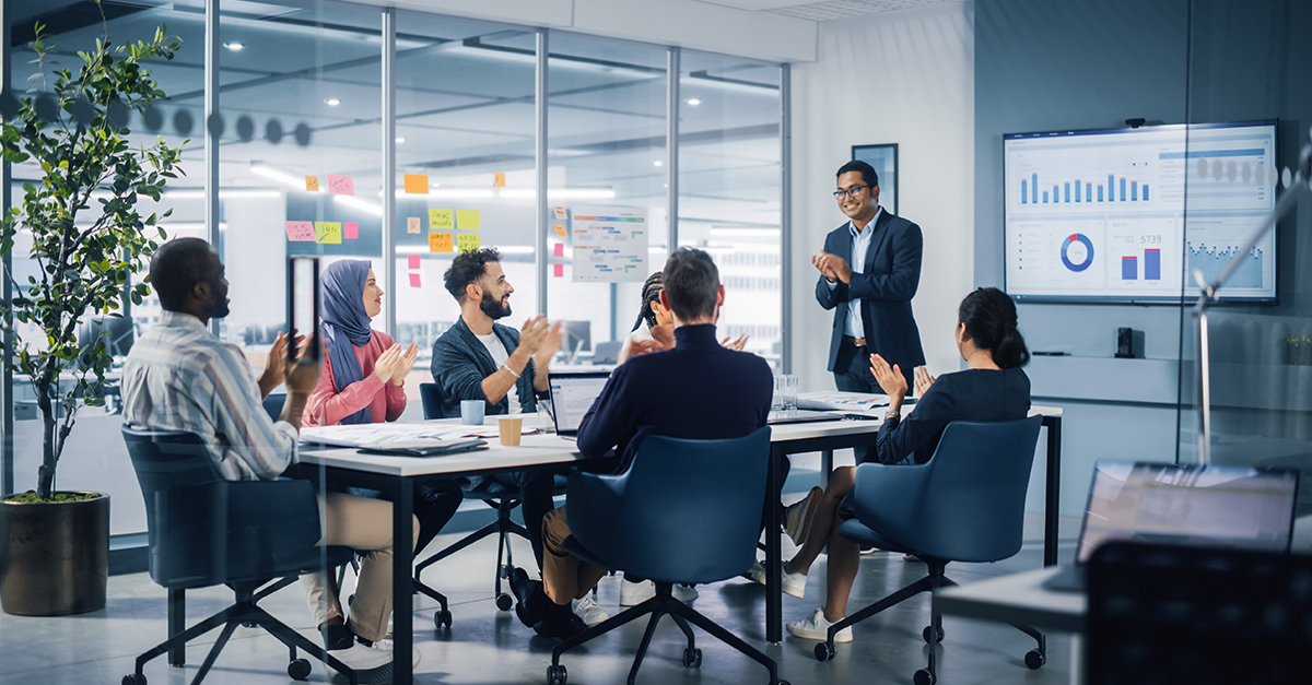 Multi-ethnic professionals in a conference room with man giving a work presentation in English