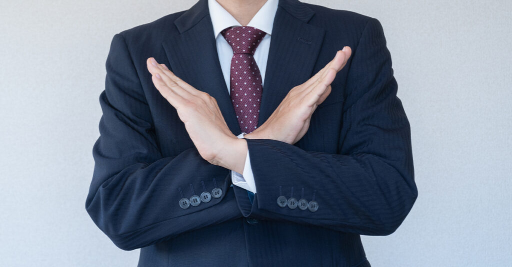 Closeup, cropped image of a man in a suit with his arms and hands crossed in a gesture of refusal, illustrating the blog topic "Formal Ways of Saying No in Spanish"