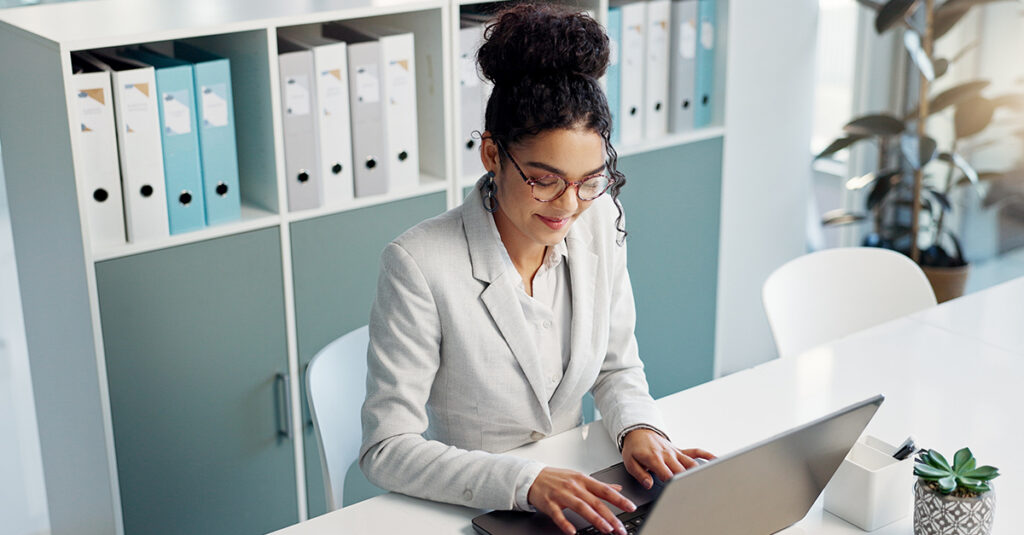Woman in a bright, contemporary office writing business emails in Spanish on a laptop