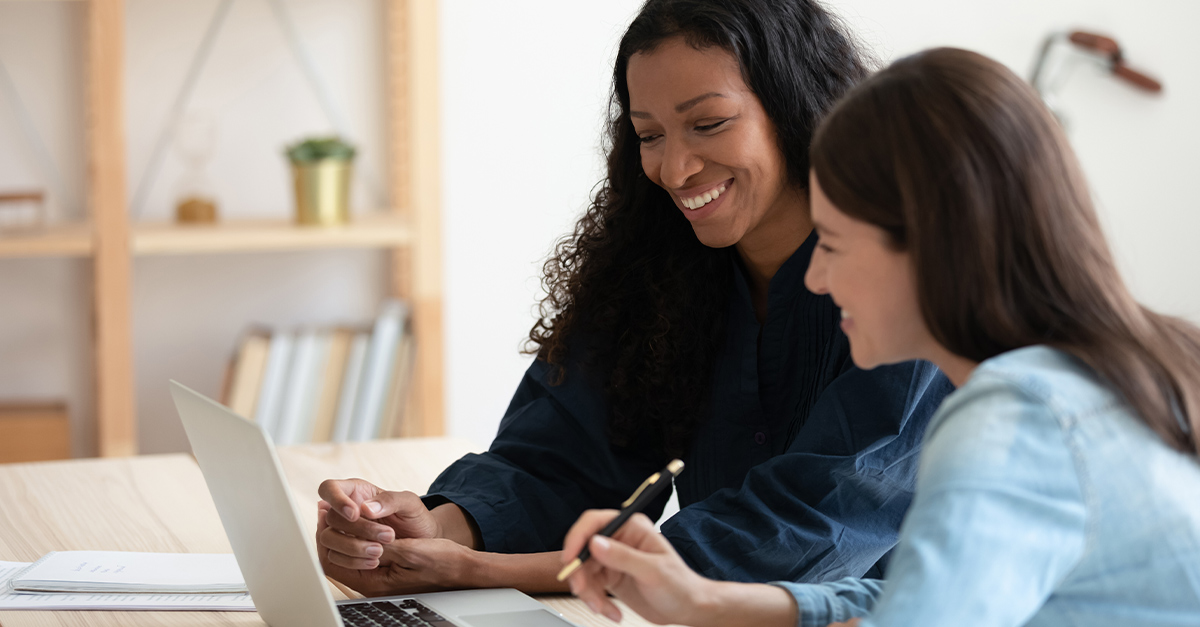 Female manager and employee looking at a laptop together during a performance review, illustrating the blog topic "Creative Ways to Turn Performance Reviews into Language Growth Opportunities"