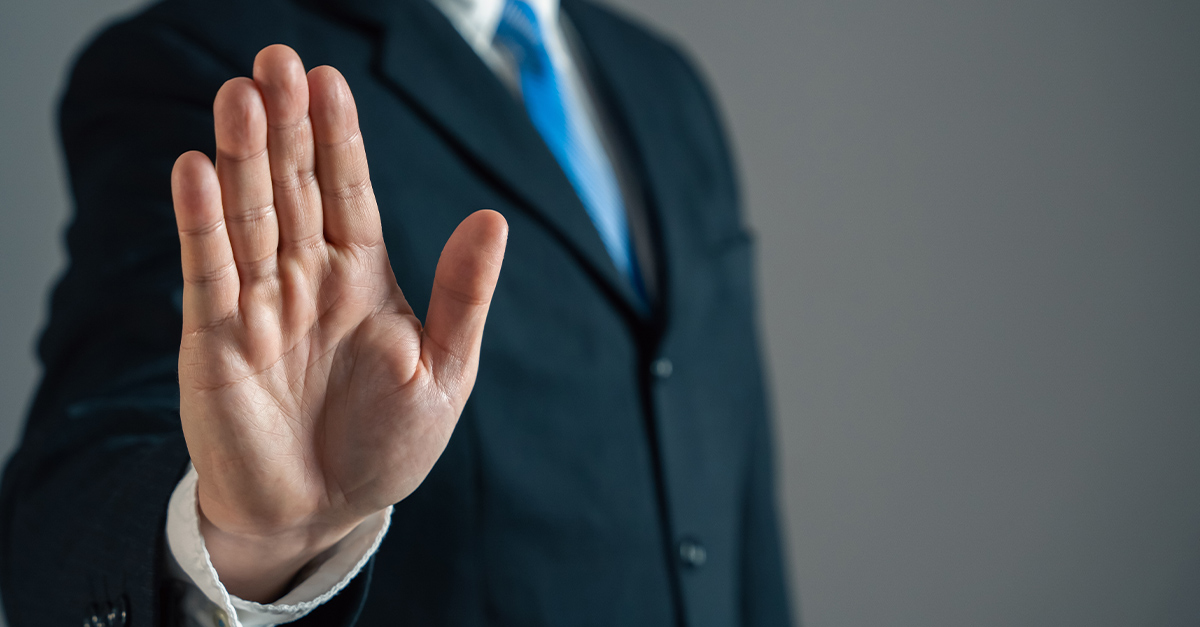 Cropped image of a man in a suit with his hand towards the camera in a "stop" gesture, illustrating the blog topic "How Multilingual Leaders Navigate Conflict More Effectively"