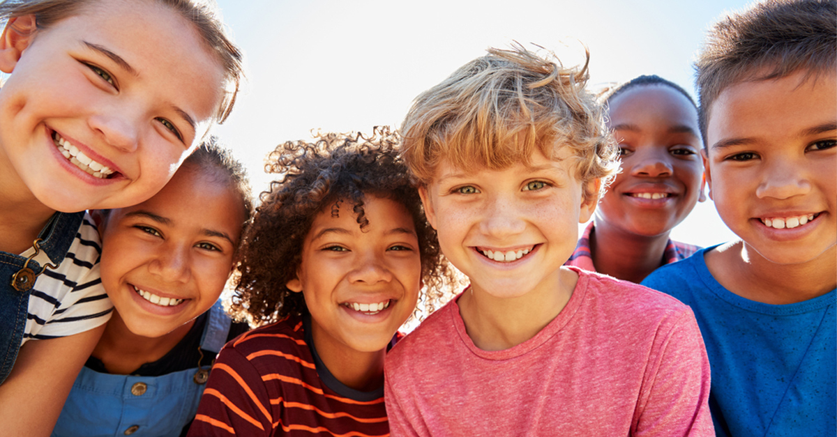 Closeup shot from below of six children huddled together looking down on the camera and smiling.