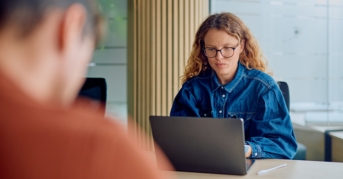 Woman with eyeglasses focused on her laptop, busy working at a desk in a contemporary office space