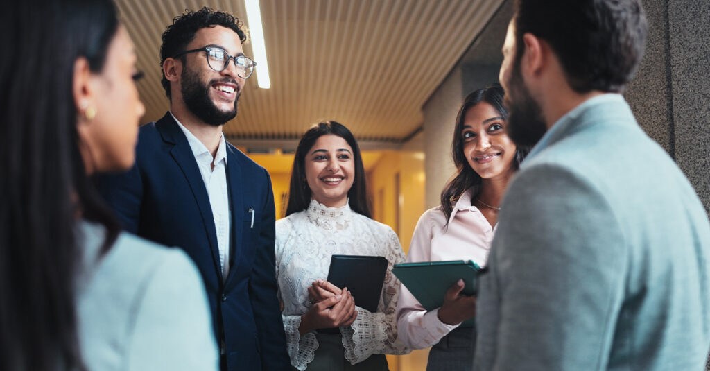 Multilingual work team standing in an office hallway, smiling and having a discussion