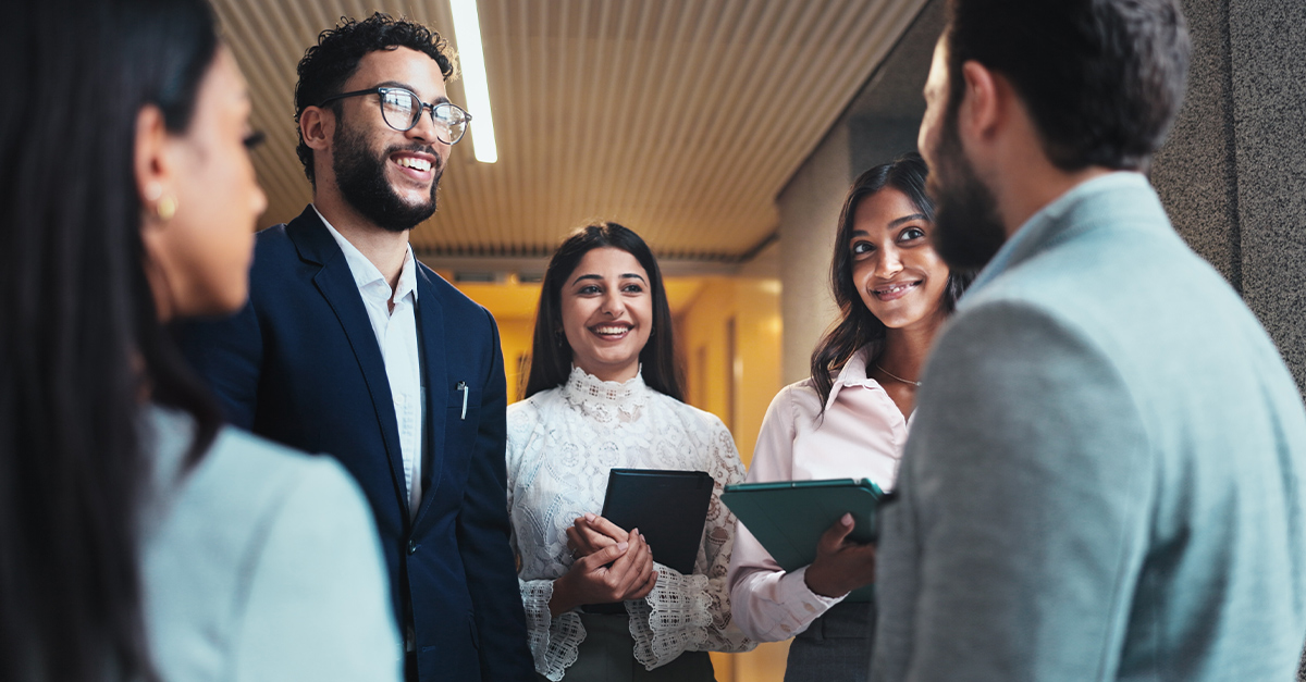 Multilingual work team standing in an office hallway, smiling and having a discussion